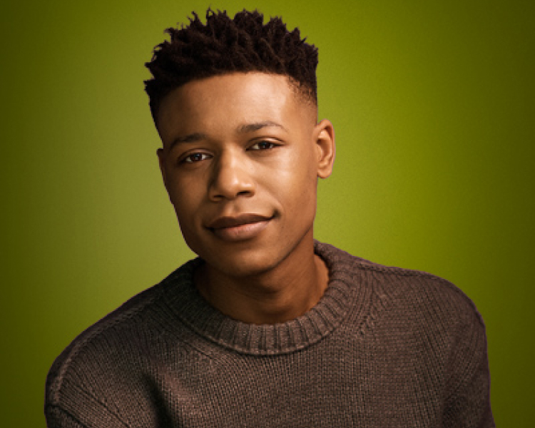 Portrait of a young Black male wearing a brown sweater.